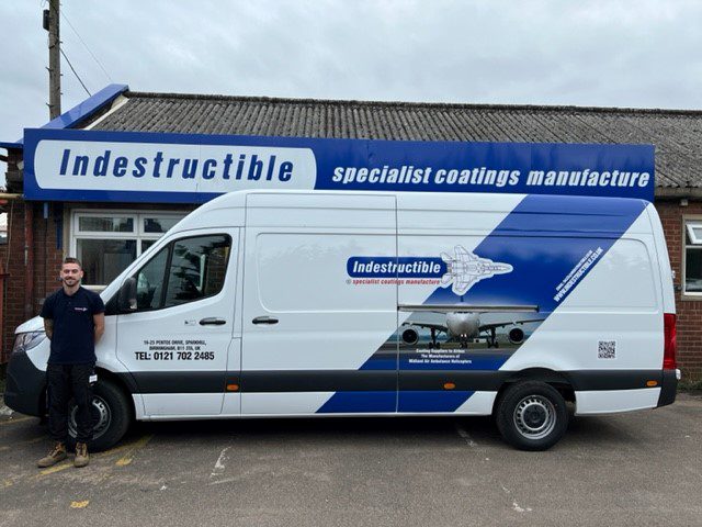 A man stands in front of a white van with a blue and white livery